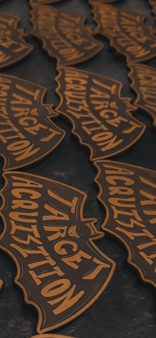 Close-up of 'Targe Acquisizione' branded leather patches on a dark background